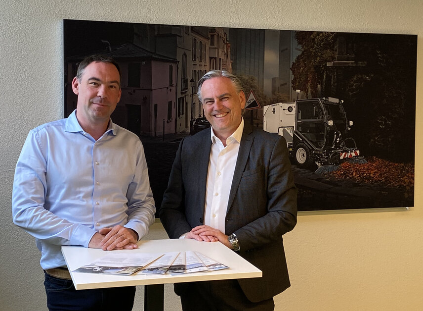 Henning Schröder (left) and Gerhard Neudorfer at the headquarters of the Aebi Schmidt Group. Behind them is a picture of a Schmidt Flexigo, our smallest all season allrounder, serving also as an example for the future of larger machines. 